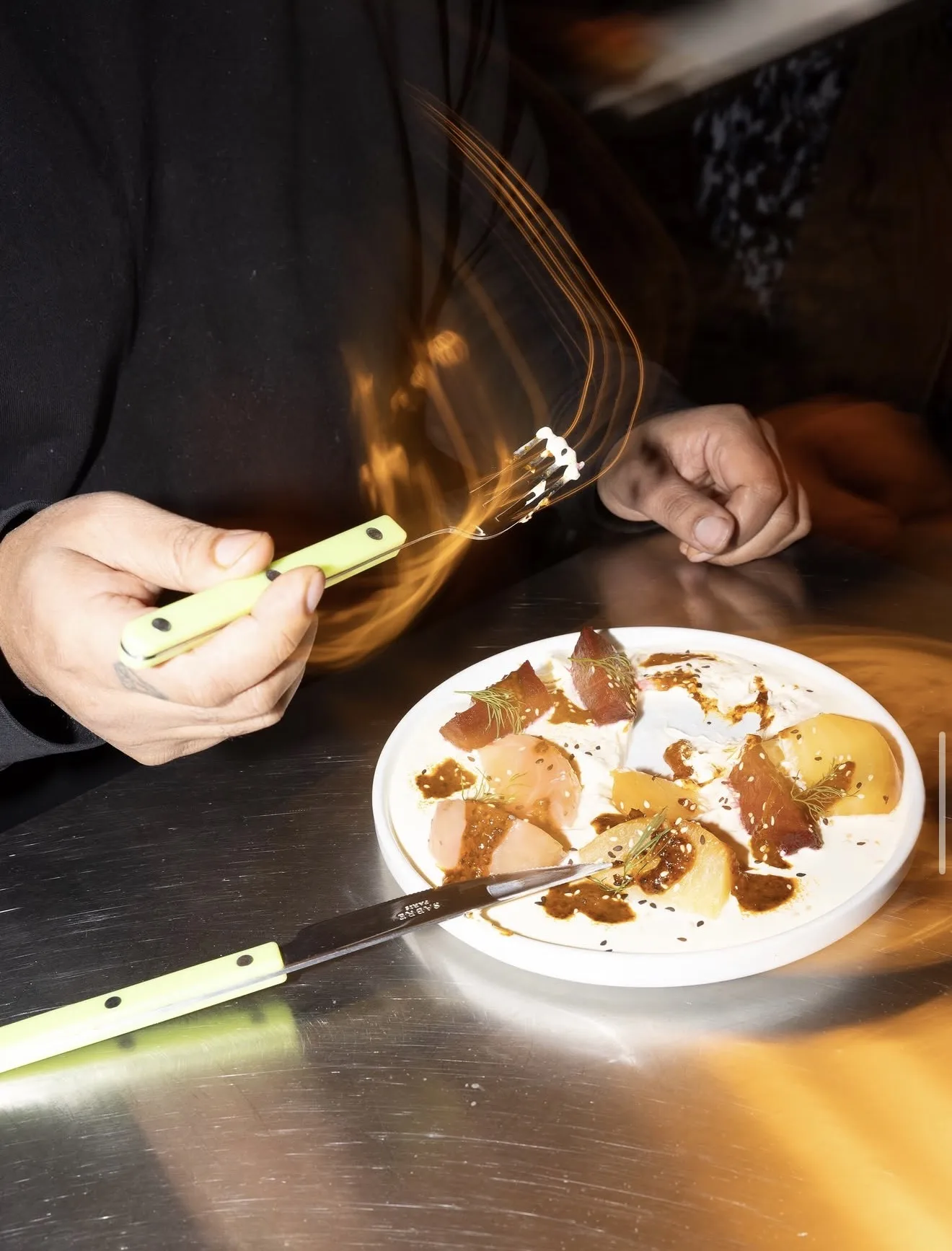 A chef plating a citrus crudo dish with a light trail from the fork