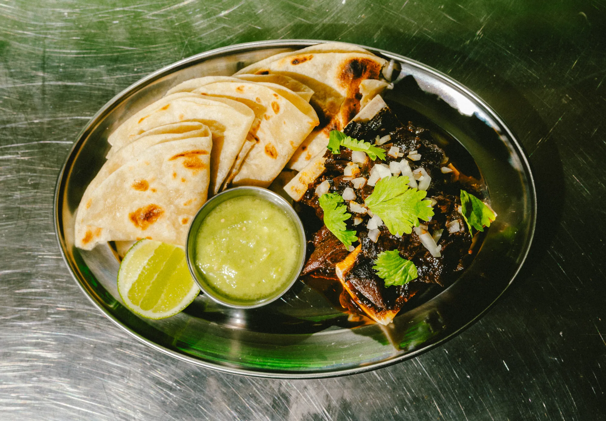 Birria with quesadillas, lime and salsa verde on a metal plate